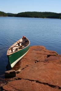 Green canoe on the shore of smooth red rock.