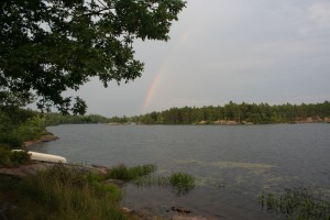 Canoe on shore with rainbow across the lake