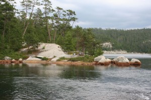 Across a bay view of smooth rocks and trees on a campsite.