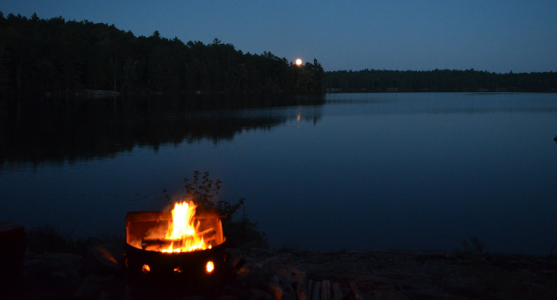 campfire, lake and full moon at treeline