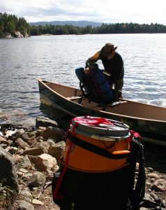 Man putting pack in a canoe with barrel on shore