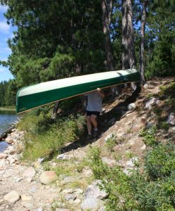 Man carrying canoe down a hill to a lake.