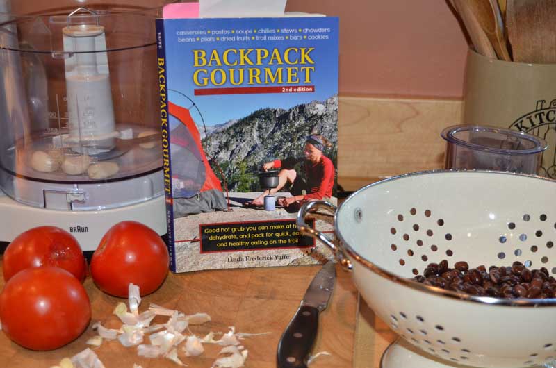 backpack gourmet cookbook surrounded by tomatos and a food processer and beans