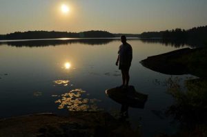man on rocks by lake with sunrise