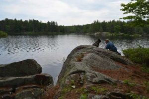 Woman and dog on rocks overlooking lake.