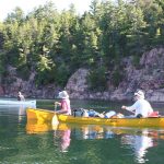 yellow and white canoe on green water and pink rock.