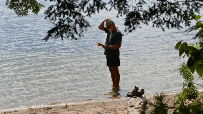 man in the water on a beach reading