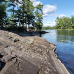 Shoreline of rock with an island in the distance.